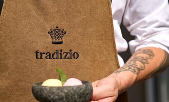 A waiter is holding a bowl with three different flavors of ice cream. He is wearing a brown apron with the logo "tradizio". | © Hotel Tradizio | © Annette Sandner