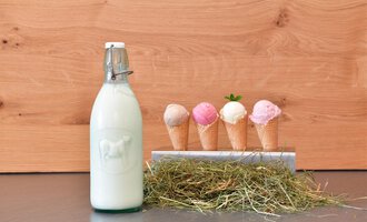 Eine Flasche Milch steht neben Waffeln mit verschiedenen Eissorten. Die Waffeln sind bunt und auf einem rustikalen Hintergrund präsentiert. | © Hotel Neue Krone GmbH | Werbewind GmbH