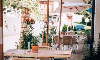 Ein gemütlicher Außenbereich eines Cafés mit Tischen und Stühlen unter Sonnenschirmen. Umgeben von Pflanzen und einer einladenden Atmosphäre. | © Hotel Neue Krone GmbH | Werbewind GmbH