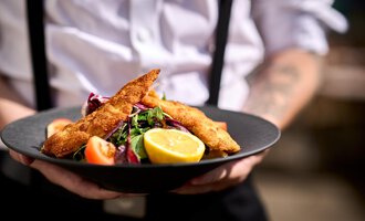 Ein Teller mit knusprigen Fischfilets, serviert auf einem Bett aus frischem Salat. Dazu gibt es Zitronenscheiben und eine Garnitur aus Tomaten. | © Hotel Tradizio | © Annette Sandner