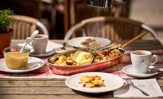 Ein rustikales Frühstück mit Kaiserschmarrn, Eis und frischen Früchten. Dazu eine Tasse Kaffee und ein Glas Pudding auf einem Holztisch. | © Hotel Tradizio | © Annette Sandner