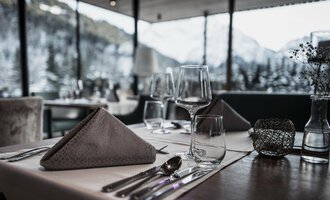 Ein elegant gedeckter Tisch in einem Restaurant mit Blick auf die verschneiten Berge. Die Atmosphäre ist gemütlich und einladend. | © Verwöhn- & Wellnesshotel Walserhof| Frank Simon