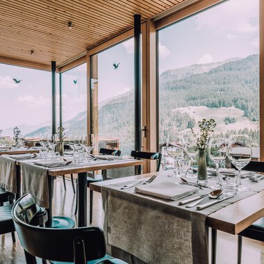 Ein modernes Restaurant mit großen Fenstern und Blick auf die Berge. Die Tische sind elegant gedeckt und schaffen eine einladende Atmosphäre. | © Naturhotel Chesa Valisa | Heldentheater