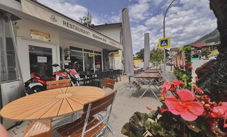 Ein Restaurant mit einer einladenden Terrasse und Holztischen. Blühende Pflanzen und ein schöner Himmel sorgen für eine angenehme Atmosphäre. | © Riezlern Eck | Sead Sulejmani
