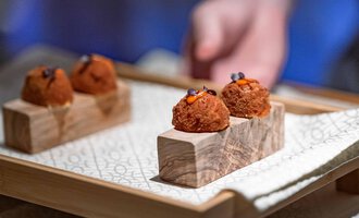 Eine stilvolle Präsentation von kleinen Köstlichkeiten auf einer Holzplatte. Die Häppchen sind mit bunten Akzenten dekoriert.