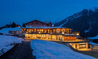 A modern building in the mountains at night, surrounded by snow. The warm lights of the decor create an inviting atmosphere. | © Hotel Birkenhöhe | GA Service Salzburg