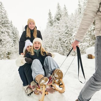 Ein Schlitten liegt im Schnee, umgeben von Bergen. Die Sonne scheint im Hintergrund und sorgt für eine winterliche Atmosphäre. | © Kleinwalsertal Tourismus | Oliver Farys