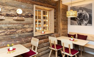 Ein gemütliches Restaurant mit Holzvertäfelung und warmem Licht. Tische und Stühle laden zum Verweilen ein, während ein Kunstwerk an der Wand die Atmosphäre ergänzt. | © Schönegger Käse-Alm