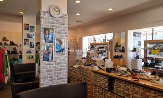 A cozy shoe store with various shoes and clothing. Photos are hanging on the wall, and a clock is visible. | © Schuhhaus Schuster | Marietta Diehl