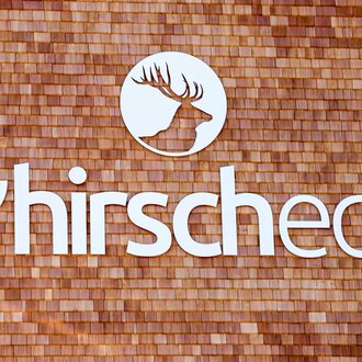 © Kleinwalsertal Tourismus | Frank Drechsel Ein Logo mit dem Namen "s'hirschcheck" ist auf einer Holzoberfläche angebracht. Das Design zeigt ein stilisiertes Geweih in einem runden Ausschnitt. | © Kleinwalsertal Tourismus | Frank Drechsel