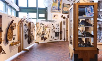 Ein Ausstellungsraum mit historischen Werkzeugen und Waffen an den Wänden. In einer Vitrine sind weitere Objekte ausgestellt. | © Kleinwalsertal Tourismus | Oliver Farys