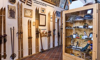 Eine Ausstellung mit mehreren Holzskiern, die an Wänden ausgestellt sind. Im Hintergrund sind Fotos und Informationen über die Skigeschichte sichtbar. | © Kleinwalsertal Tourismus | Oliver Farys