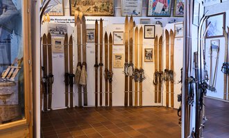 Eine Ausstellung mit alten Skiern und Ausrüstung. Die Wände sind mit historischen Informationen und Bildern dekoriert. | © Kleinwalsertal Tourismus | Oliver Farys