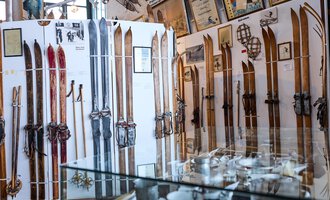 Eine Ausstellung mit verschiedenen alten Skiern an den Wänden. Im Vordergrund sind Glaskästen mit weiteren Sammlerstücken zu sehen. | © Kleinwalsertal Tourismus | Oliver Farys