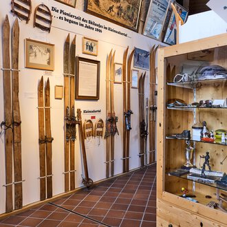 An exhibition featuring several wooden skis displayed on walls. In the background, photos and information about ski history are visible. | © Kleinwalsertal Tourismus | Oliver Farys