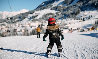 Zwei Skifahrer gehen einen schneebedeckten Weg entlang. Im Hintergrund sind Bäume und eine klare, blaue Himmel sichtbar. | © Kleinwalsertal Tourismus | Oliver Farys