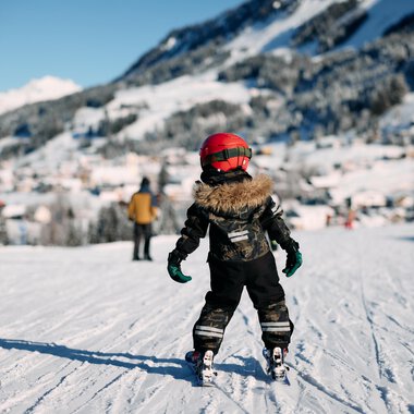 Zwei Skifahrer gehen einen schneebedeckten Weg entlang. Im Hintergrund sind Bäume und eine klare, blaue Himmel sichtbar. | © Kleinwalsertal Tourismus | Oliver Farys