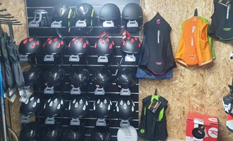 Eine Wand mit mehreren Helmen und Anzügen für Sportaktivitäten. Die Helme sind schwarz mit roten Akzenten, während die Anzüge in verschiedenen Farben gehalten sind. | © IFA Hotel Alpenrose