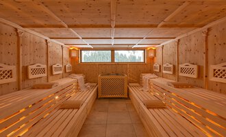 Ein gemütlicher Saunaraum aus hellem Holz mit Bänken und indirekter Beleuchtung. Durch die Fenster hat man einen Blick ins Grüne. | © Aparthotel Kleinwalsertal Haller GmbH & Co KG