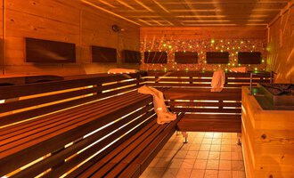 Eine moderne Sauna mit Holzbank und sanfter Beleuchtung. Entspannungsbereich mit mehreren Sitzen und dekorativem Licht. | © Aparthotel Kleinwalsertal Haller GmbH & Co KG