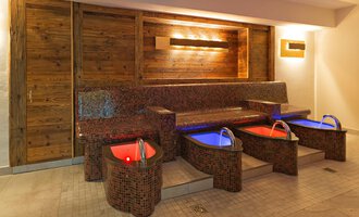 Ein eleganter Wellnessbereich mit vier Fußbädern und einer gemütlichen Sitzbank. Die sanfte Beleuchtung sorgt für eine entspannte Atmosphäre. | © Aparthotel Kleinwalsertal Haller GmbH & Co KG