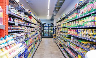 A narrow aisle in a supermarket with shelves full of groceries. On both sides, various kinds of canned goods and sauces are arranged. | © SPAR