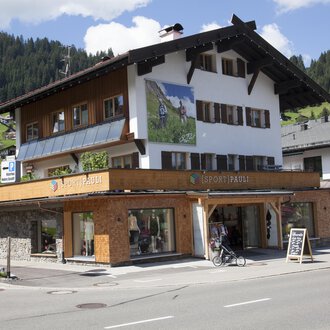 Ein traditionelles Alpenhaus mit Holzverkleidung und großen Fenstern. Im Vordergrund befindet sich ein Fahrrad und ein Informationsschild. | © Sport Pauli Matthias Bischof e.U