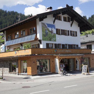 A traditional alpine house with wooden cladding and large windows. In the foreground is a bicycle and an information sign. | © Sport Pauli Matthias Bischof e.U