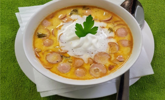 A delicious soup with slices of sausage and a creamy cream topping. Fresh herbs garnish the dish.