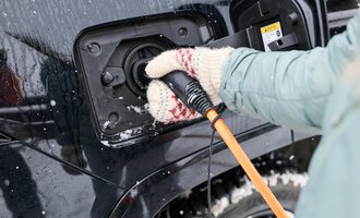 Eine Person steuert ein Ladekabel in die Ladebuchse eines Autos. Es liegt Schnee und die Person trägt warme Handschuhe. | © Kleinwalsertal Tourismus | Oliver Farys