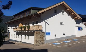 Ein modernes Gebäude mit einem Balkon und einem Parkplatz. Die Fassade ist hell und freundlich, umgeben von Bergen. | © Kleinwalsertal Tourismus