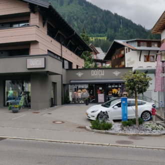 Ein modernes Geschäft in den Bergen mit einer stilvollen Fassade. Vor dem Laden steht ein weißes Auto und es sind bunte Fahnen sichtbar.
