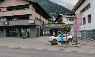 Ein modernes Geschäft in den Bergen mit einer stilvollen Fassade. Vor dem Laden steht ein weißes Auto und es sind bunte Fahnen sichtbar.