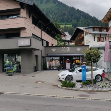 Ein modernes Geschäft in den Bergen mit einer stilvollen Fassade. Vor dem Laden steht ein weißes Auto und es sind bunte Fahnen sichtbar.