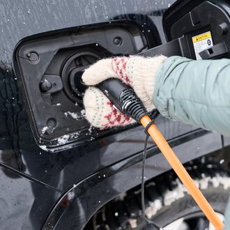 A person plugs a charging cable into an electric vehicle. It is snowing and the hand is equipped with a warm glove. | © Kleinwalsertal Tourismus | Oliver Farys