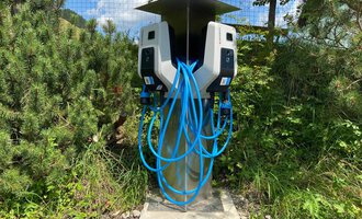 Eine moderne Ladestation für Elektrofahrzeuge mit mehreren Ladeanschlüssen. Umgeben von grüner Vegetation und unter einem sonnigen Himmel. | © Kleinwalsertal Tourismus