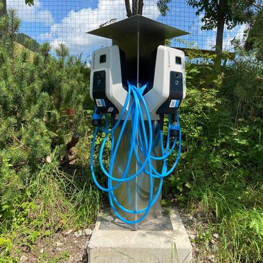 Eine moderne Ladestation für Elektrofahrzeuge mit mehreren Ladeanschlüssen. Umgeben von grüner Vegetation und unter einem sonnigen Himmel. | © Kleinwalsertal Tourismus
