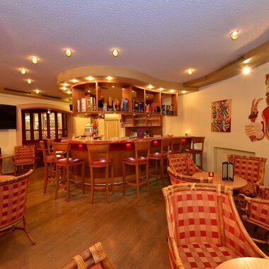Eine gemütliche Bar mit einladenden Stühlen und einer warmen Beleuchtung. Im Hintergrund befindet sich eine gut gefüllte Bar und bunte Wandkunst. | © IFA Hotel Alpenhof Wildental