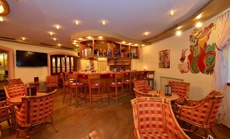 Eine gemütliche Bar mit einladenden Stühlen und einer warmen Beleuchtung. Im Hintergrund befindet sich eine gut gefüllte Bar und bunte Wandkunst. | © IFA Hotel Alpenhof Wildental