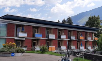 Ein modernes Gebäude mit mehreren Balkonen in einer grünen Umgebung. Im Hintergrund sind Berge und ein blauer Himmel zu sehen. | © Kleinwalsertal Tourismus | Veronika Senn