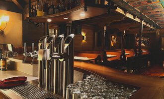 Eine gemütliche Bar mit mehreren Zapfhähnen und einem gut sortierten Getränkeangebot. Im Hintergrund sind Holztische und ein warmes Ambiente zu sehen. | © Taverne | Sead Sulejmani