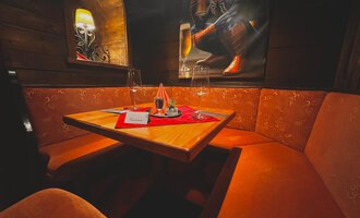 Ein gemütlicher Tisch in einer einladenden Ecke mit orangefarbenen Sitzbänken. Auf dem Tisch stehen Gläser und eine dekorative Serviette. | © Taverne | Sead Sulejmani
