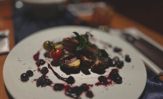 Ein kunstvoll angerichteter Teller mit Fleisch, Beeren und Gemüse. Die kreative Sauce verleiht dem Gericht einen ansprechenden Look. | © Taverne | Sead Sulejmani