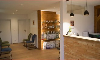 Ein moderner Empfangsbereich mit Holzverkleidung und eleganten Lampen. Aufregende Regale zeigen verschiedene Produkte, und die Sitze sind bereit für Besucher. | © Tierarztpraxis Oberstdorf | Regina Baumgartner