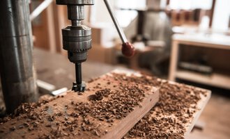 A wood drill is working on a piece of wood. Wood shavings are scattered across the workbench. | © Türtscher Die Schreinermanufaktur