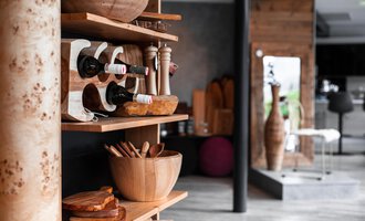 Ein stilvolles Regal mit Weinflaschen, Holzgeschirr und Küchenutensilien. Im Hintergrund sind moderne Möbel und eine ansprechende Raumgestaltung zu sehen. | © Türtscher Die Schreinermanufaktur