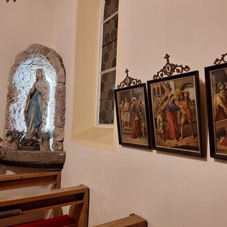 Eine Kirchengalerie mit einer Statue von Maria und mehreren historischen Gemälden an der Wand. Die Atmosphäre ist friedlich und andächtig. | © Unterwestegg-Kapelle Maria Hilf | Tanja Ritsch