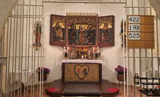 Ein geschützter Altarraum mit einem dekorativen Altarschrein und Kerzen. Die Wand ist schlicht, und es stehen einige Blumen im Vordergrund. | © Unterwestegg-Kapelle Maria Hilf | Tanja Ritsch