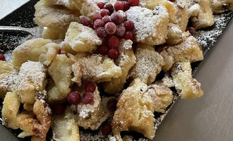 A plate with baked dough, sprinkled with powdered sugar and red berries. There is a bowl of applesauce on the side. | © Uusziit | Chantal Kessler