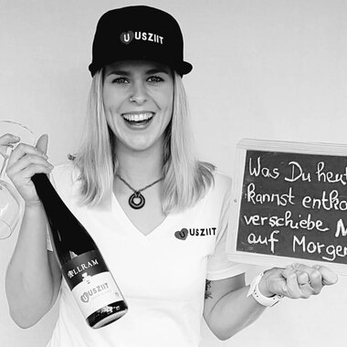 Eine fröhliche Frau hält ein Glas und eine Flasche Sekt in der Hand. Sie steht neben einer Tafel mit der Aufschrift: "Was Du heute kannst entfernen, verschiebe NICHT auf Morgen!!". | © Uusziit | Chantal Kessler